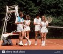 1970s-1980s-two-couples-wearing-white-tennis-clothes-standing-on-court-G6CFWF.jpg