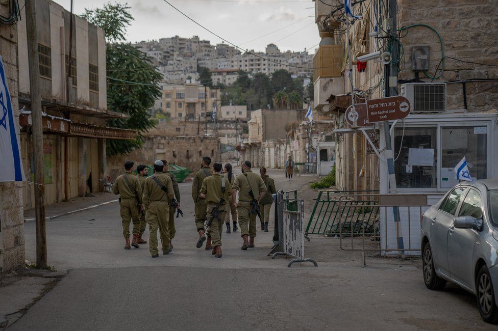 Israeli soldiers walk past Fawaz Qafisha's house. The Palestinian residents are not allowed on the street.'s house. The Palestinian residents are not allowed on the street.