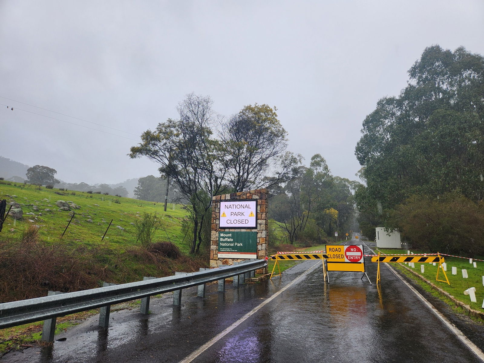 Yellow and black signs saying road closed barricade off a wet road with a sign saying national park closed.