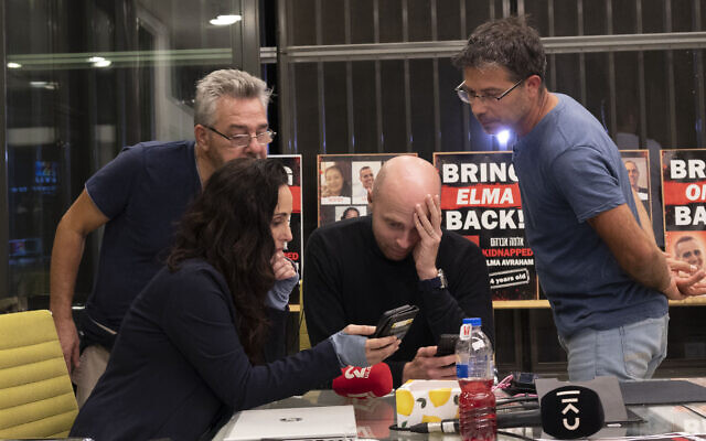 Amir Tibon, second from right, grips his head with emotion as he watches a picture of Ela and Dafna Elyakim being released from Gaza on November 26, 2023, in Mishmar Haemek. (Canaan Lidor/Times of Israel)