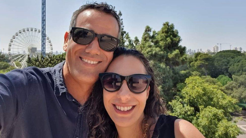 A family photo of Omri and Lishay Lavi, smiling towards the camera with a ferris wheel behind them