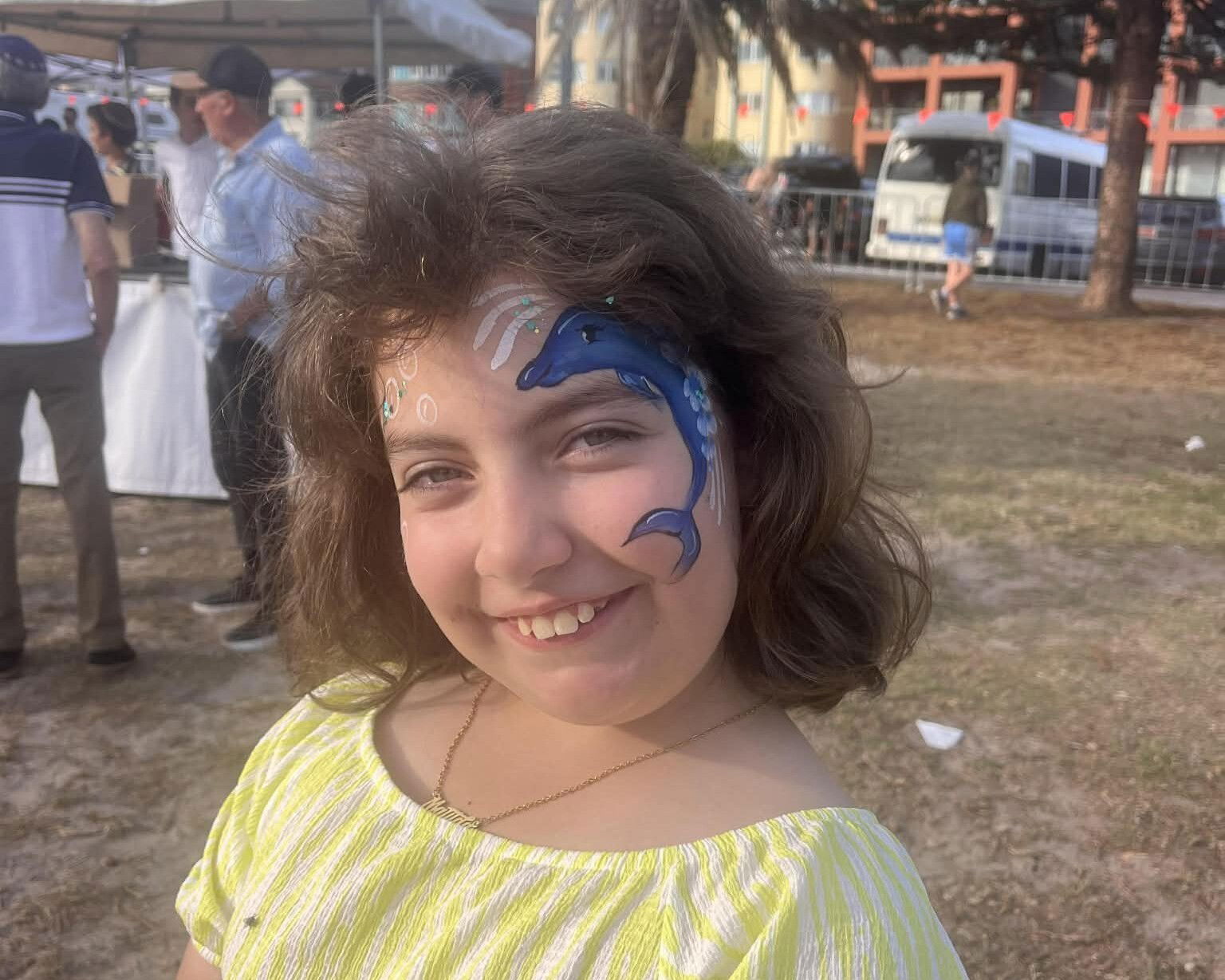 A young girl smiles with a dolphin face painting on her cheek