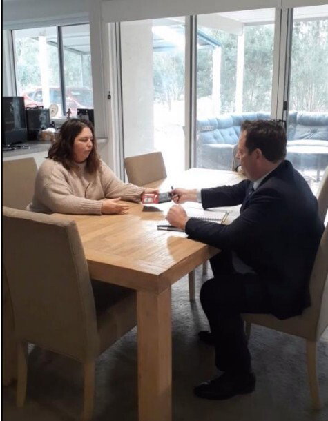 Erin Patterson hands her phone to a police officer sitting at her table.