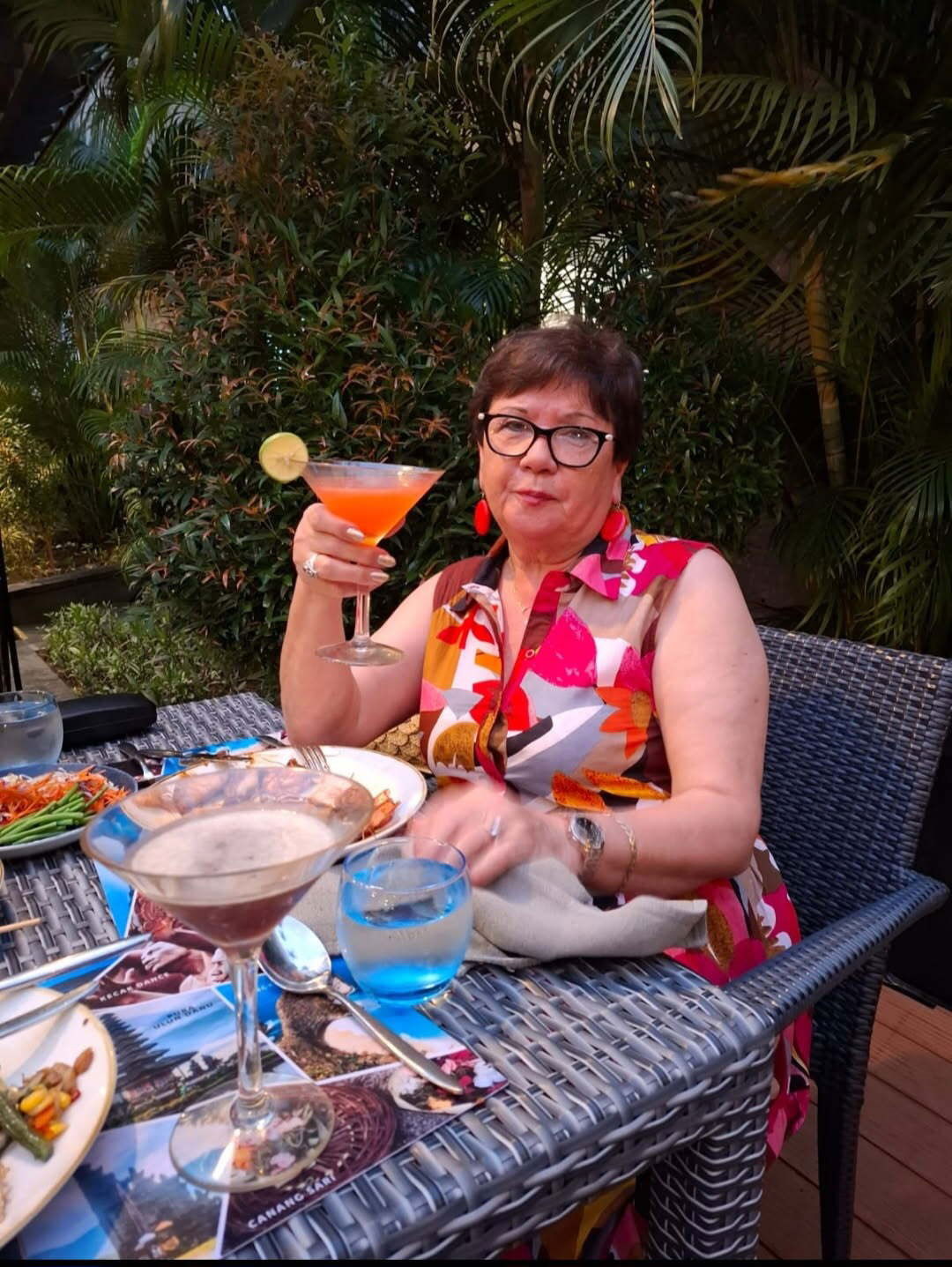 Tania Tretiak  wearing a bright dress holds up a cocktail glass.