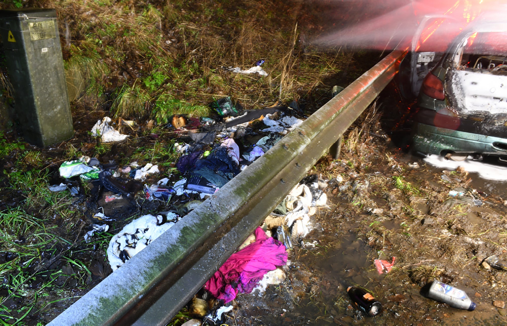 <p>Tattered clothes and bottles lay strewn on the ground next to the destroyed vehicle</p>