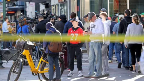 Getty Images Crowds of people gather on a New Orleans street as police tape can be seen in a blur in the foreground