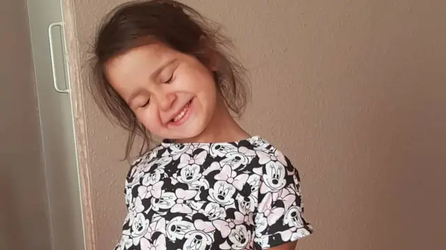 Sara, wearing Mini Mouse print pyjamas, tilts her head, closes her eyes and grins Sara, wearing Mini Mouse print pyjamas, tilts her head, closes her eyes and grins